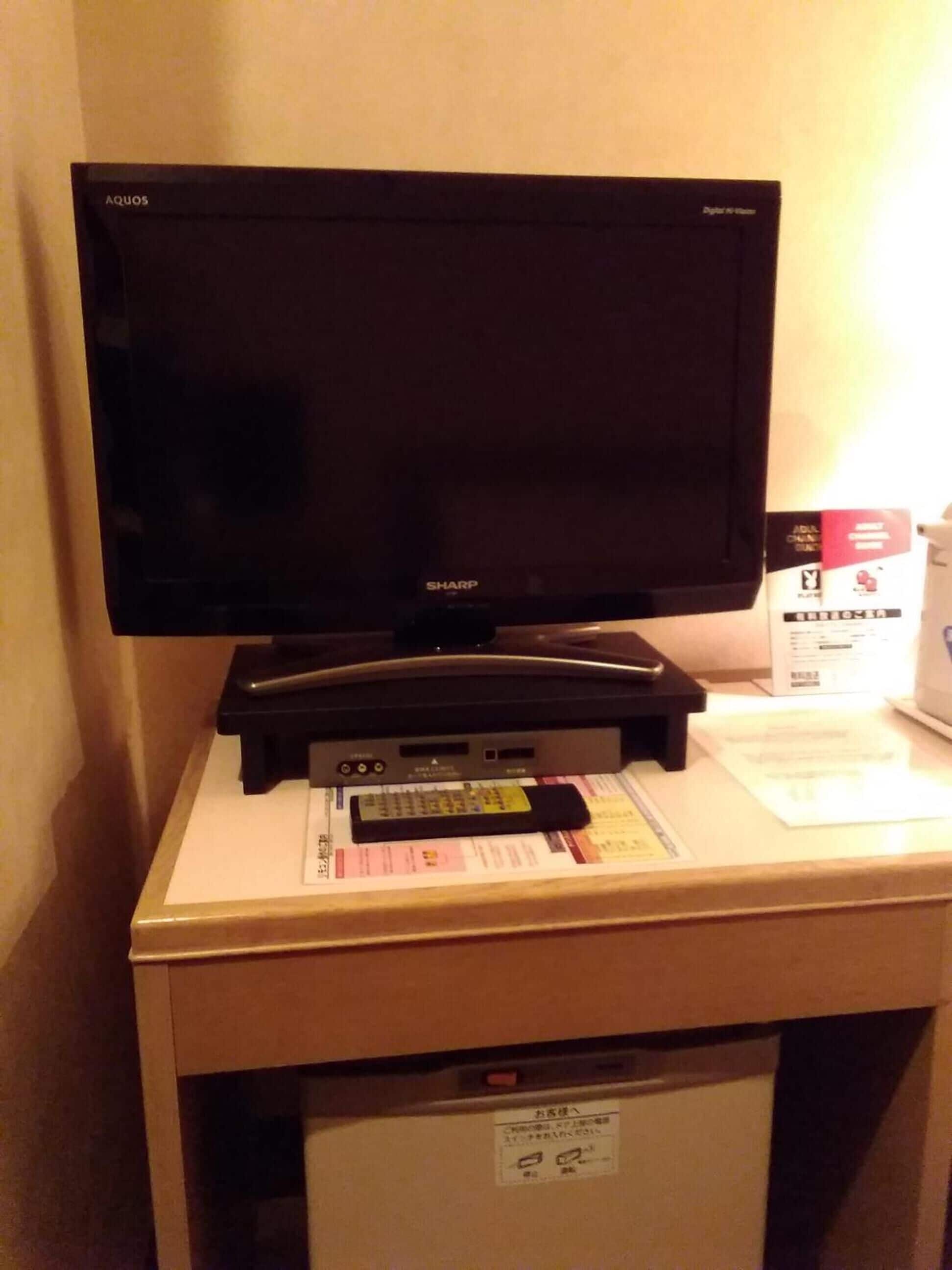 Un televisor sobre un escritorio, con un control remoto, un recibo y un refrigerador pequeño.