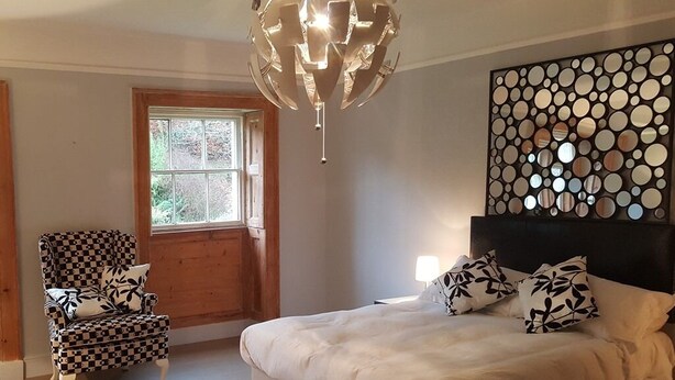 Un dormitorio con una cama grande, un sillón a cuadros, un panel decorativo en la pared y una ventana.