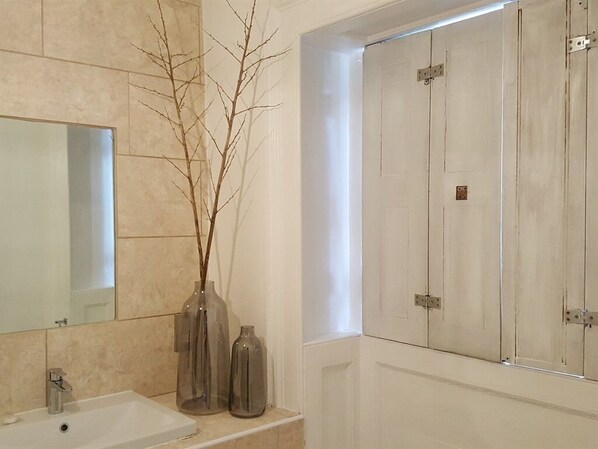 A bathroom with a white sink, mirror, and two clear vases with branches. - Grigshot Apartment (Stroud)
