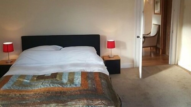 Ein Schlafzimmer mit einem Bett, zwei Nachttischen und einem Stuhl im anliegenden Raum.