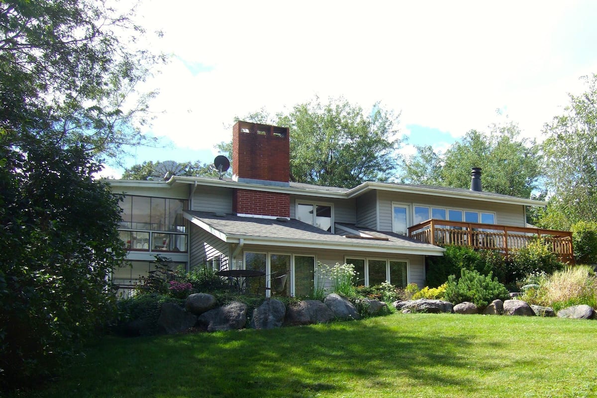 A two-story house with a brick chimney, a wooden deck, and a well-maintained lawn.