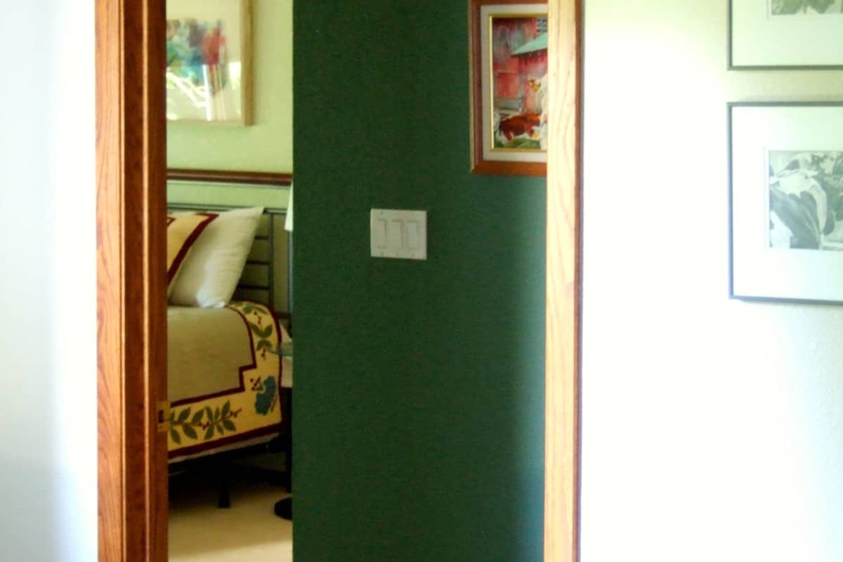 A hallway with a green wall, a wooden door frame, and a bed with patterned bedding.