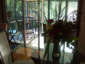 Uma sala de jantar com mesa de vidro, cadeiras e um vaso de flores.