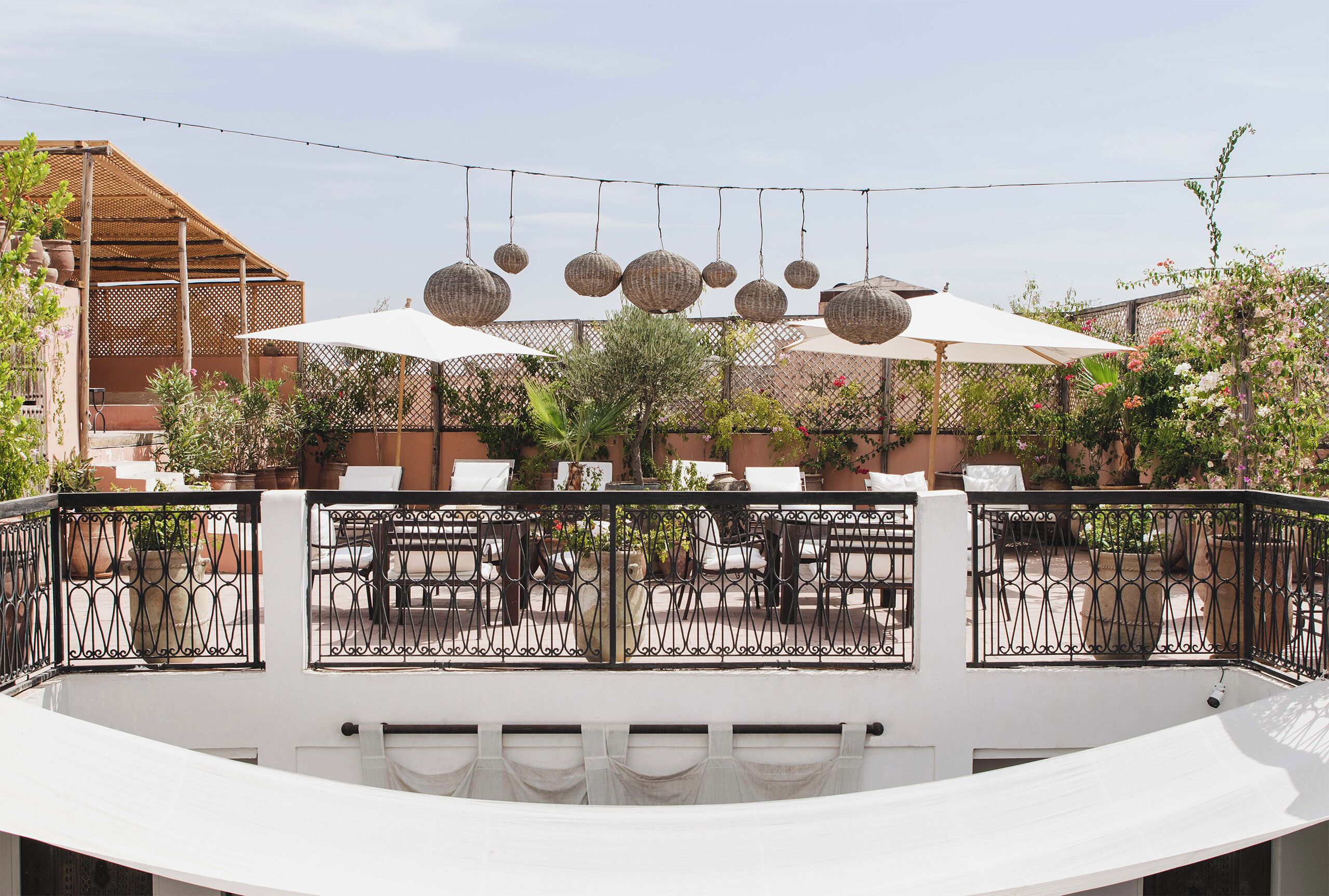 An outdoor seating area with tables and chairs, surrounded by a white wall and a black wrought iron fence.