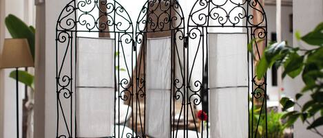 A room with a decorative metal partition featuring a mirror and a cushioned seat.
