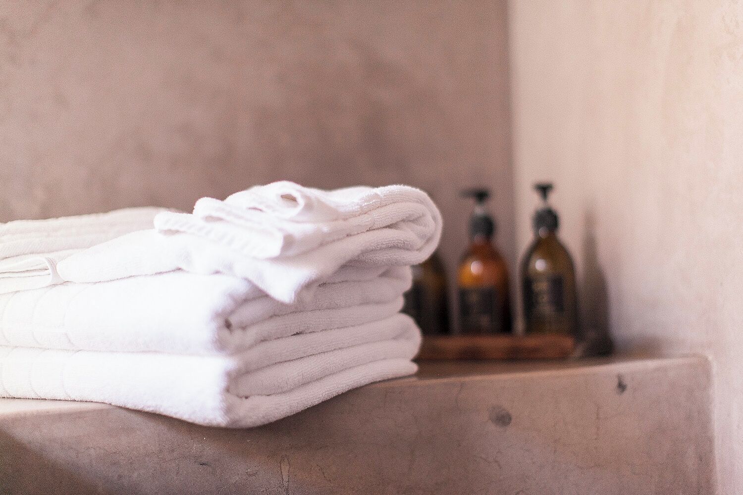 A stack of white towels on a beige surface with two bottles in the background.
