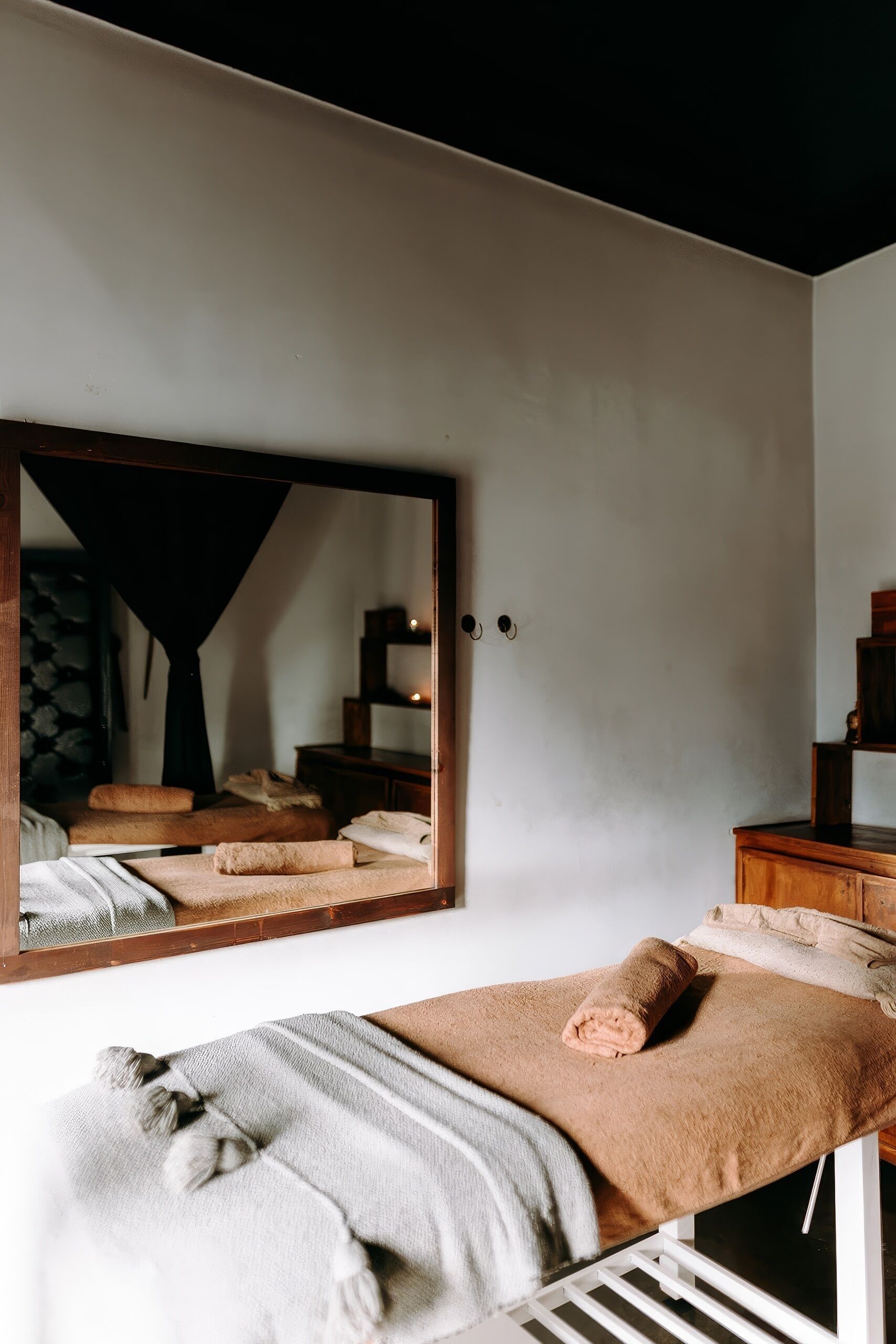 A room with a bed, a large mirror, a wooden dresser, and a small shelf.