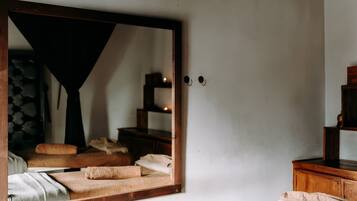 Una habitación con cama, un espejo grande, un aparador de madera y un estante pequeño.