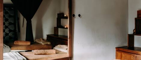 A room with a bed, a large mirror, a wooden dresser, and a small shelf.