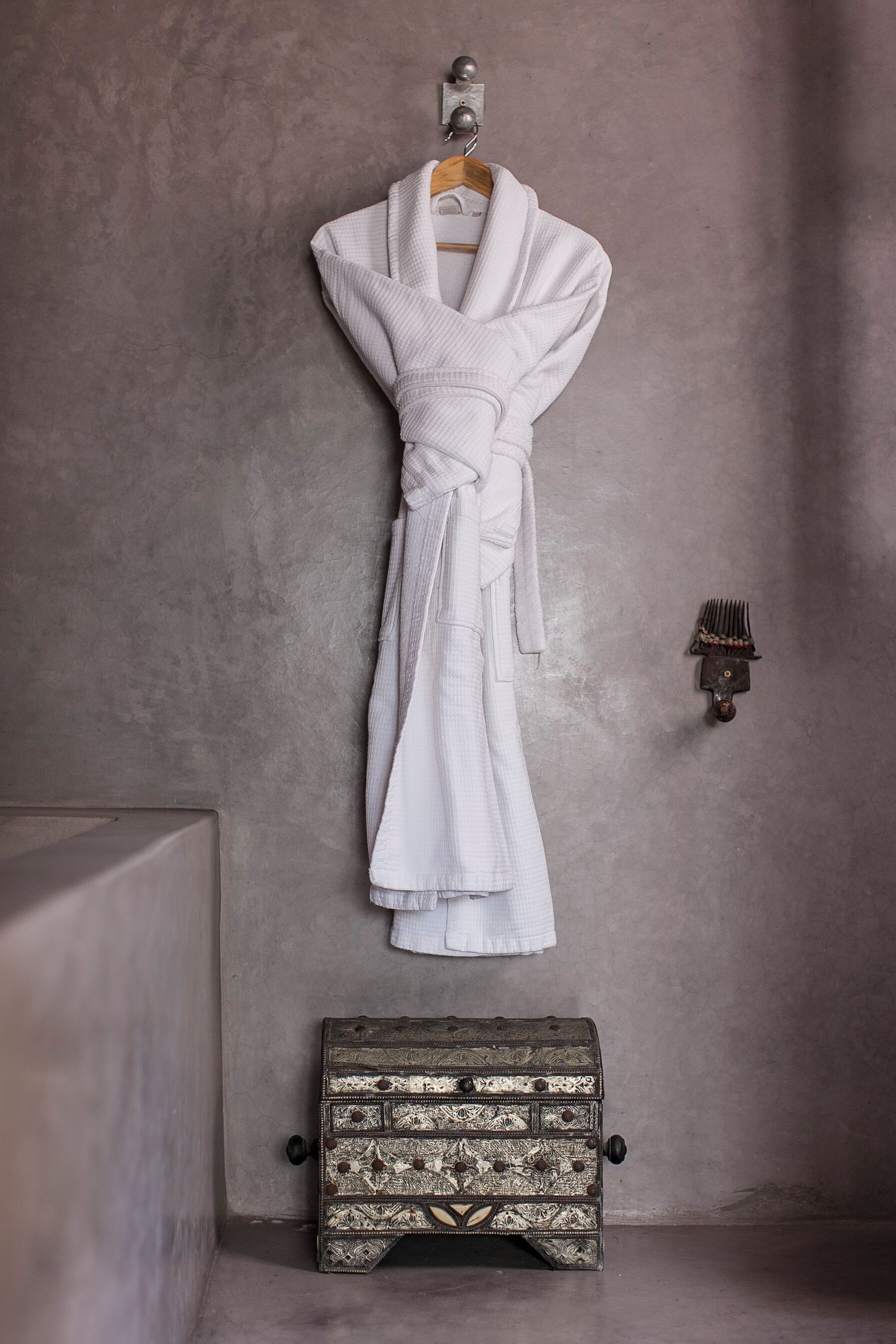 Un abito bianco appeso a un appendiabiti di legno, con un comò vintage sottostante.