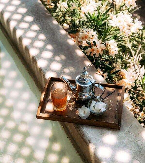 A tray with a teapot, a glass of tea, and a bowl of sugar cubes on a wooden surface.