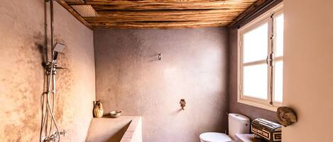 Une salle de bain rustique avec un plafond en bois, une baignoire, des toilettes et une fenêtre.