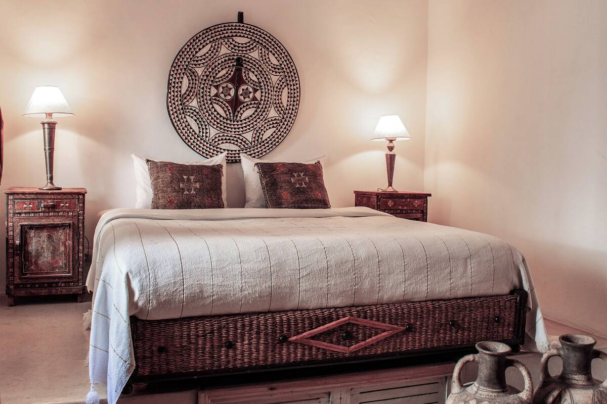 A neatly made bed with a patterned headboard, two bedside tables with lamps, and a decorative wall piece.