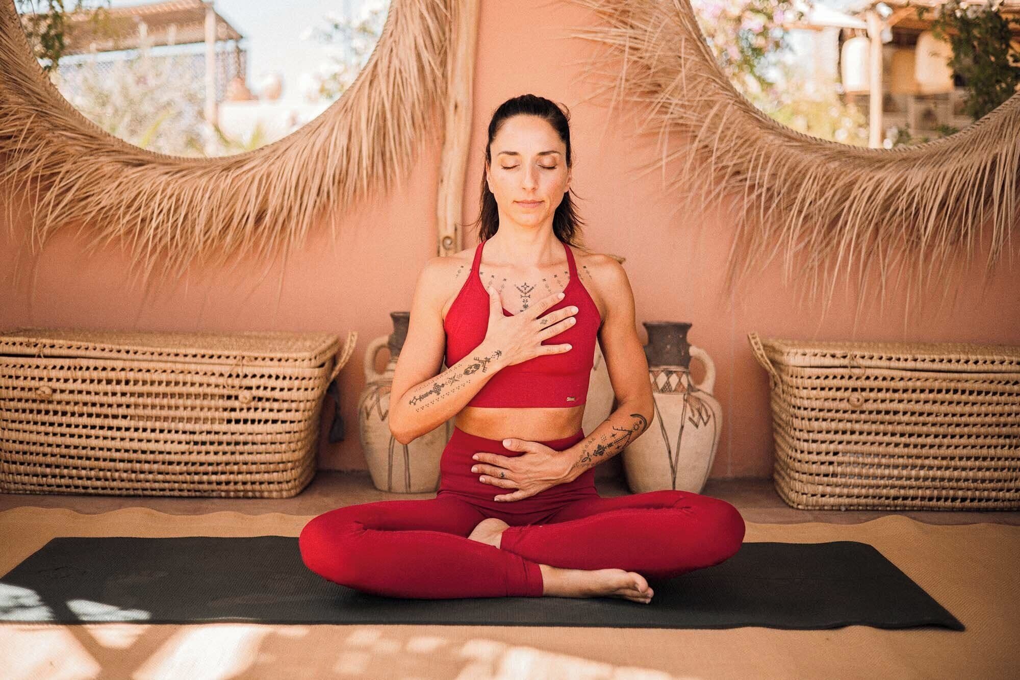 A person seated on a yoga mat in a room with woven baskets and a textured wall.