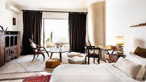 Ein Hotelzimmer mit einem Bett, einem runden Tisch, zwei Stühlen, einem Holzschrank und einem großen Fenster mit Vorhängen.