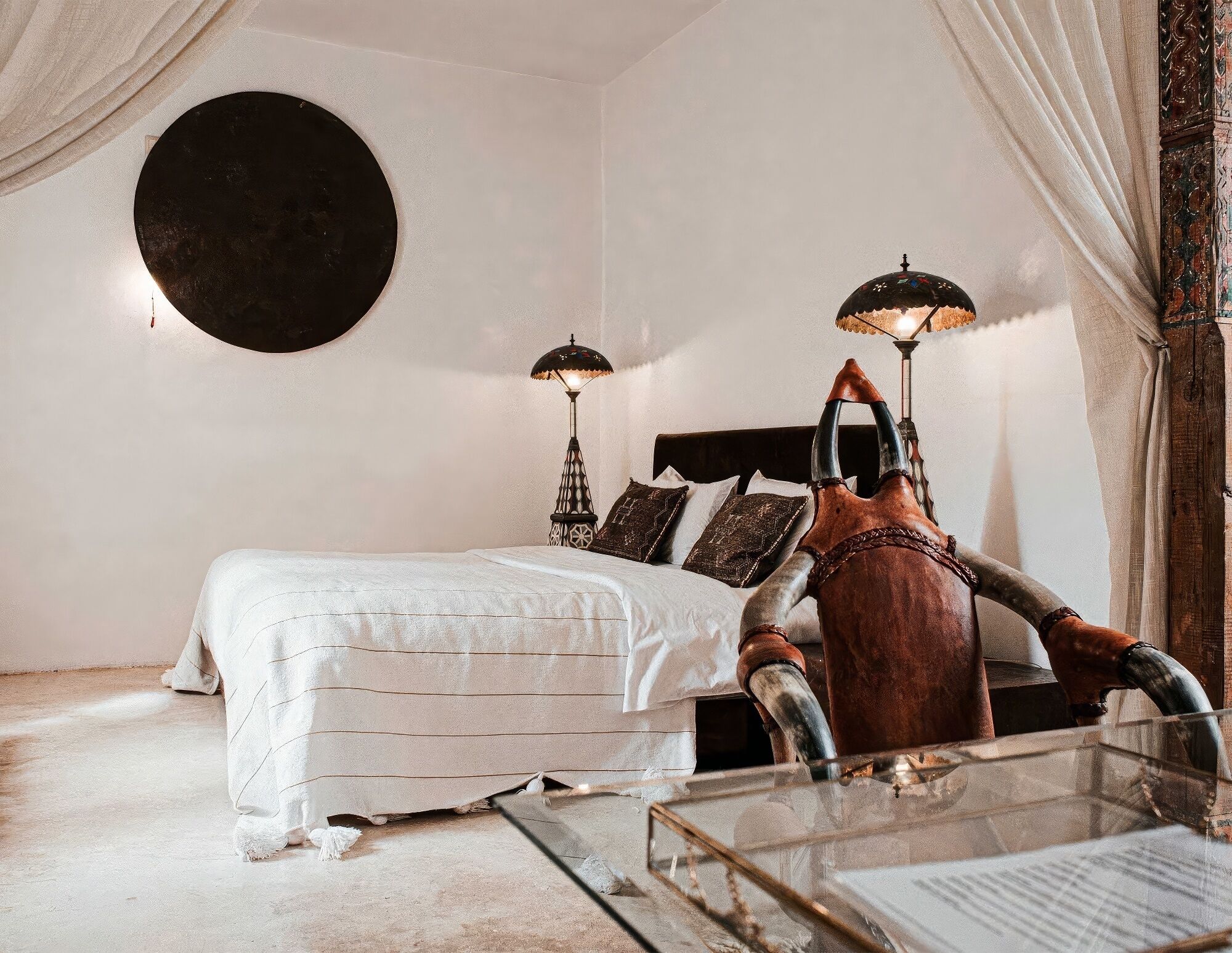 Un dormitorio con una cama, dos lámparas de pared, una cabeza de toro decorativa y un espejo redondo.