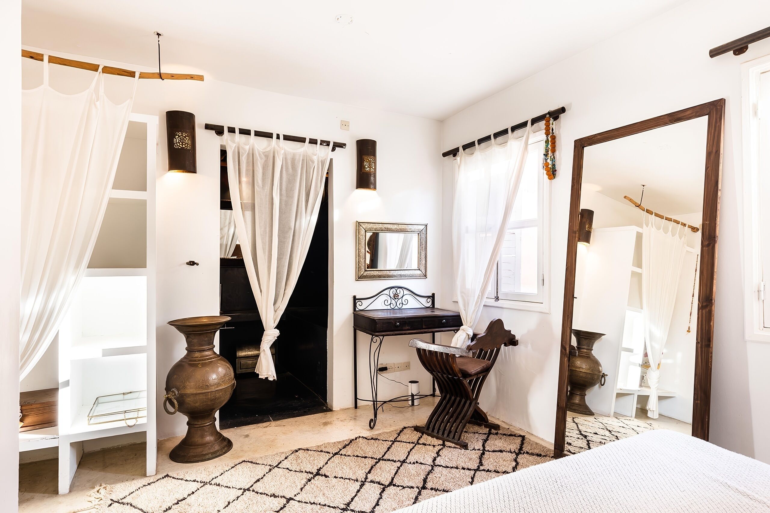 A bedroom with a bed, a vanity with a mirror, a desk, and a chair.