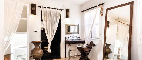 A bedroom with a bed, a vanity with a mirror, a desk, and a chair.