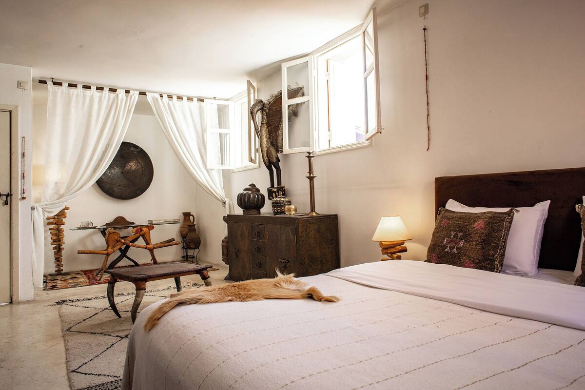 A bedroom with a bed, a wooden dresser, a lamp, and a window with curtains.