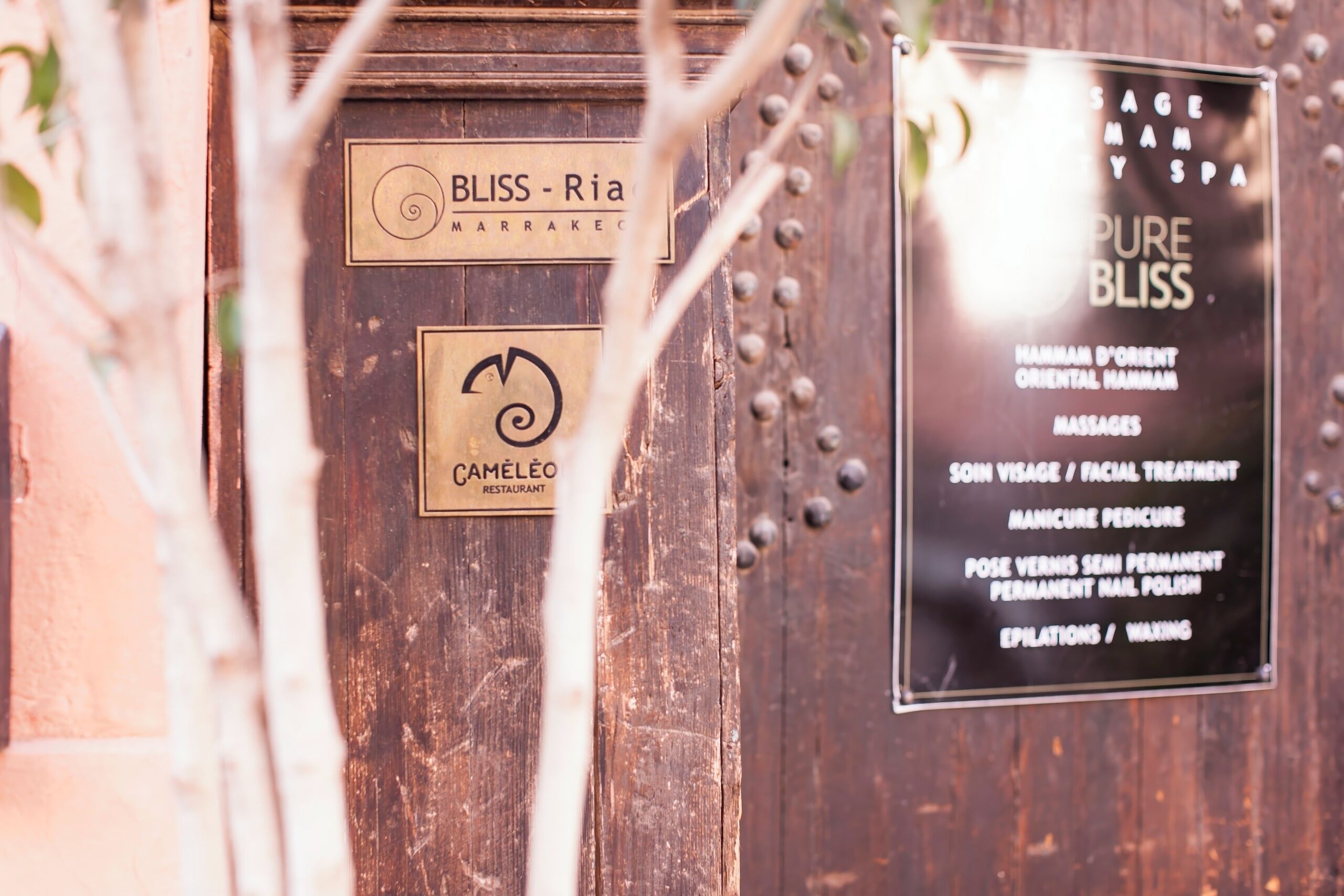 Una puerta de madera con carteles que dicen 'BLISS - Ria Marrakes' y 'RESTAURANTE CAMÉLEO'.