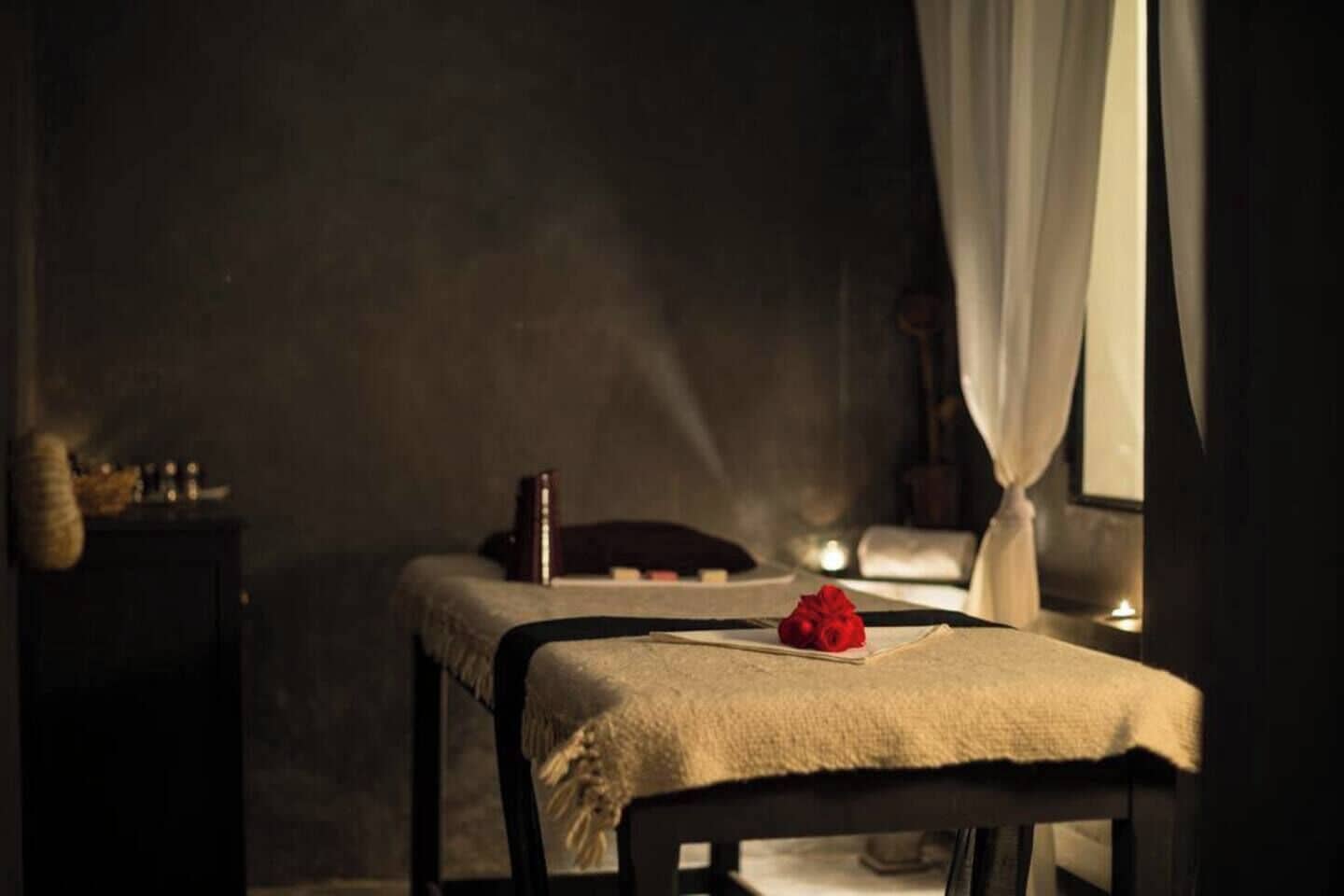 Una habitación tenue con una cama, una mesita de noche y una ventana con cortinas.