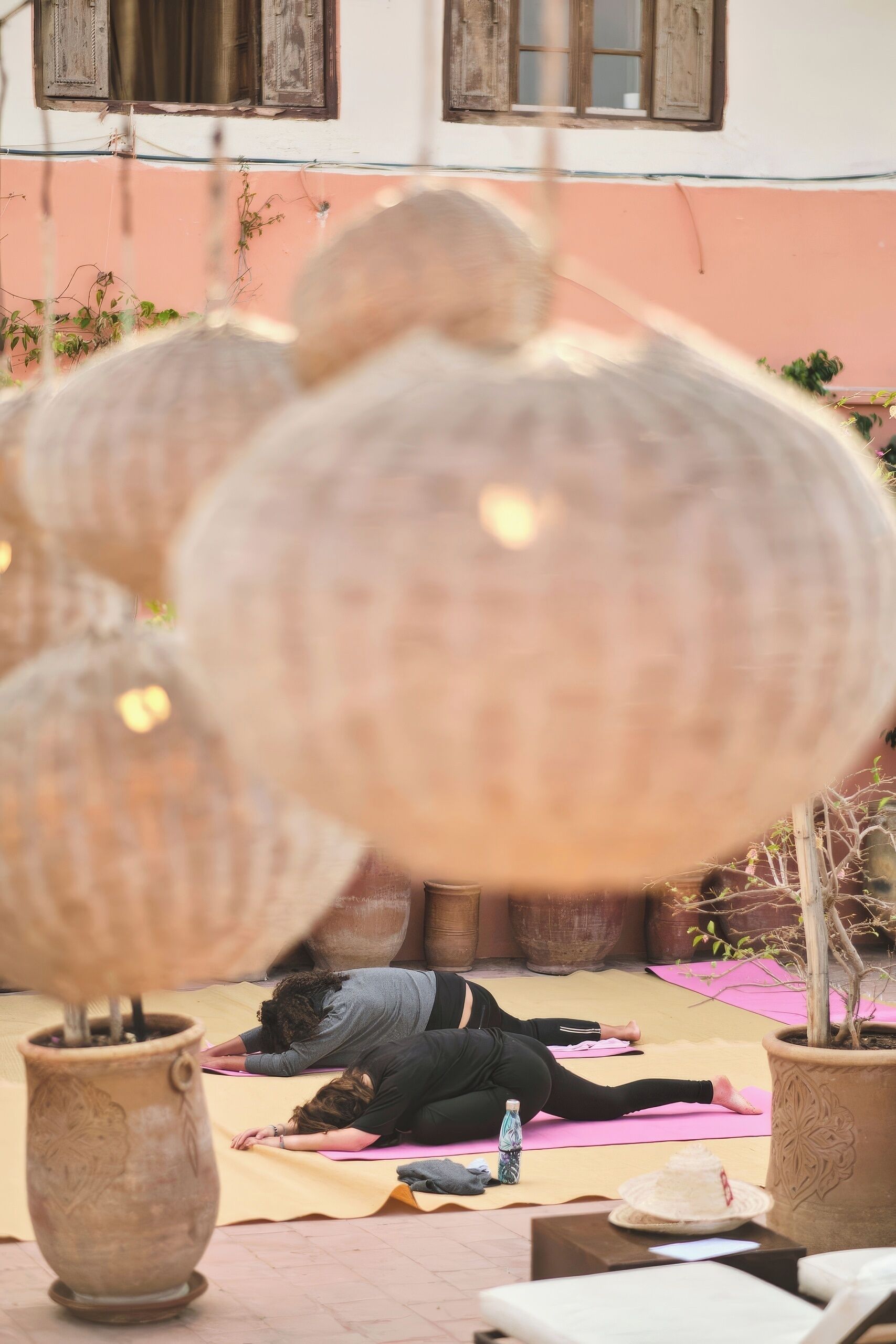 A yoga class in an outdoor setting with participants on mats, surrounded by potted plants and large vases.