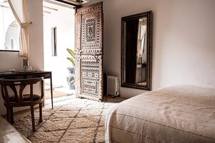 Un dormitorio con una cama, una silla de madera, un escritorio con espejo y una puerta decorativa.