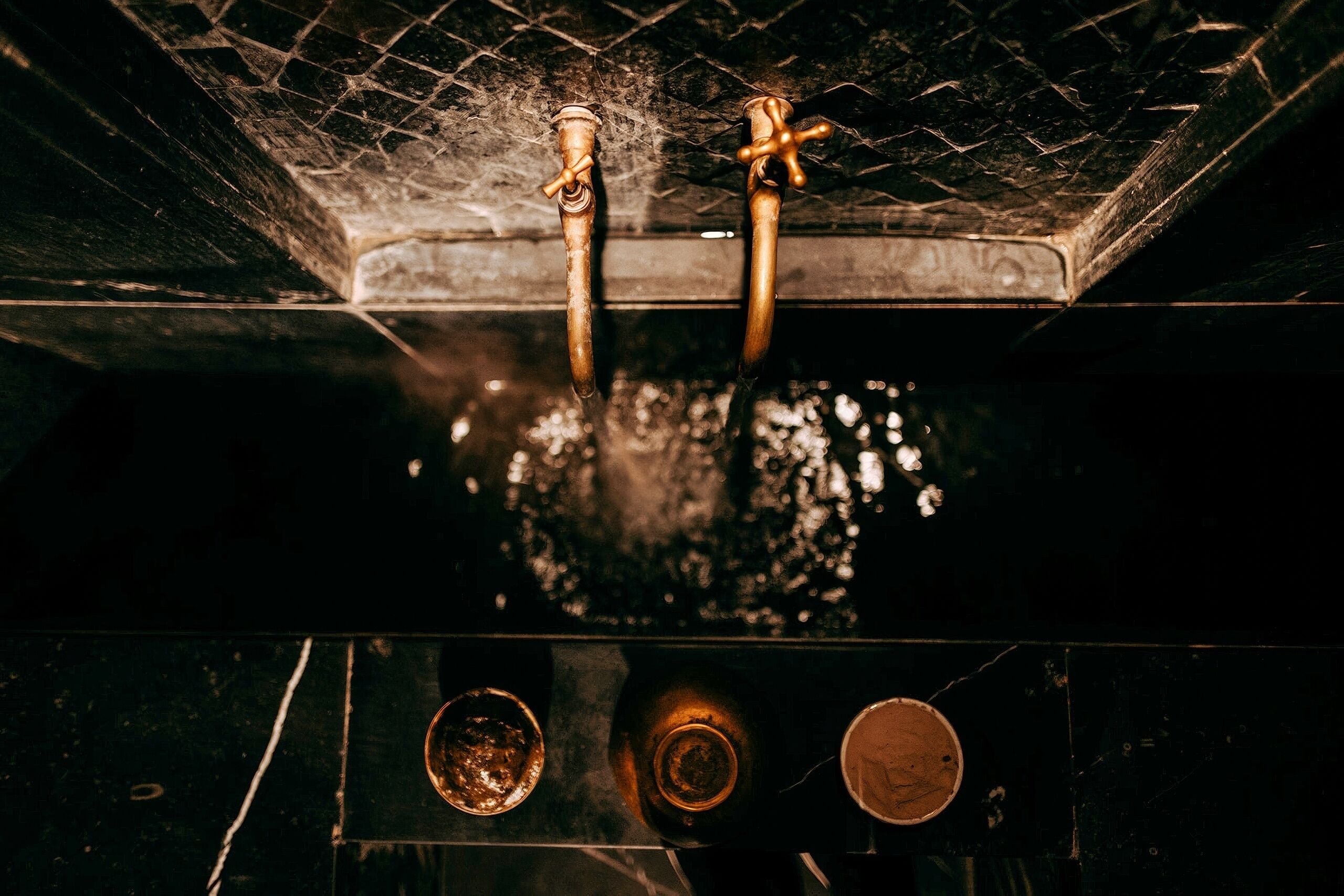 Detalle de un baño con pared oscura y con textura, y una superficie reflectante.