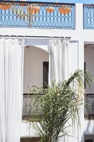 Un edificio blanco con balcón, adornado con barandillas metálicas y cortinas blancas.