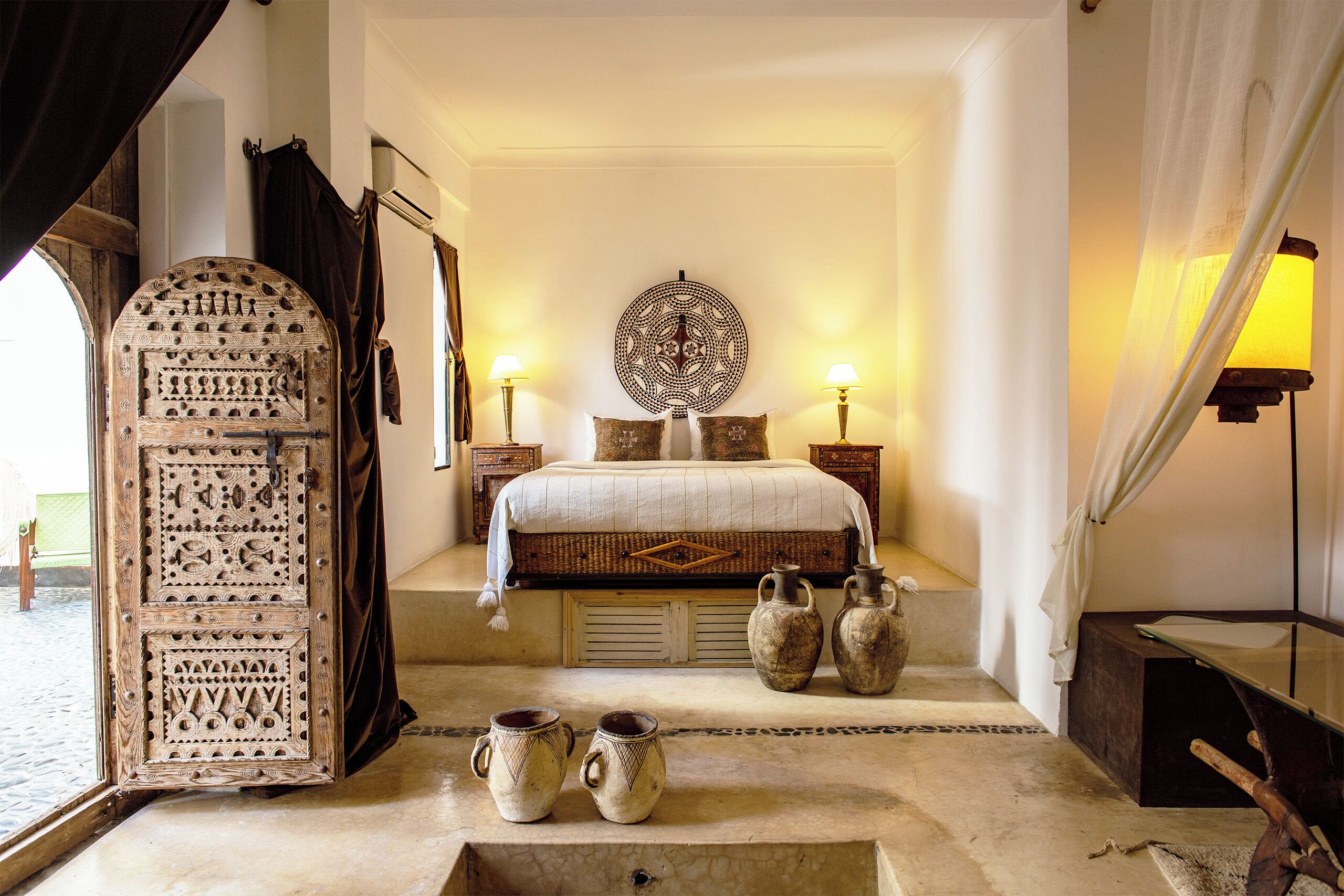 A bedroom with a bed, decorative wall art, two bedside lamps, and a large arched doorway.