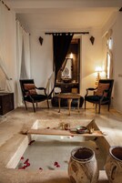 Una stanza con due poltrone, un tavolino e una conca decorativa con acqua e petali di rosa.