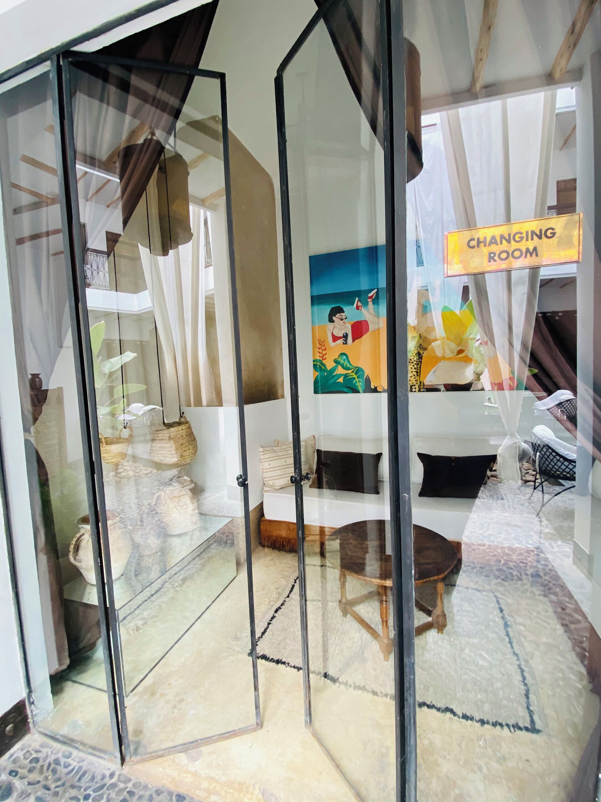 A changing room with a glass partition, a sofa, a painting, and a sign indicating the room's purpose.