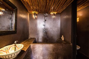 Un bagno con una grande vasca, un lavandino e un water. Sono presenti due luci a parete e uno specchio sopra il lavandino.