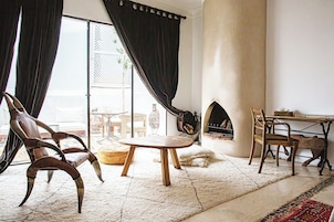 Una sala de estar acogedora con chimenea, un ventanal con cortinas, una mesa redonda y un perro.