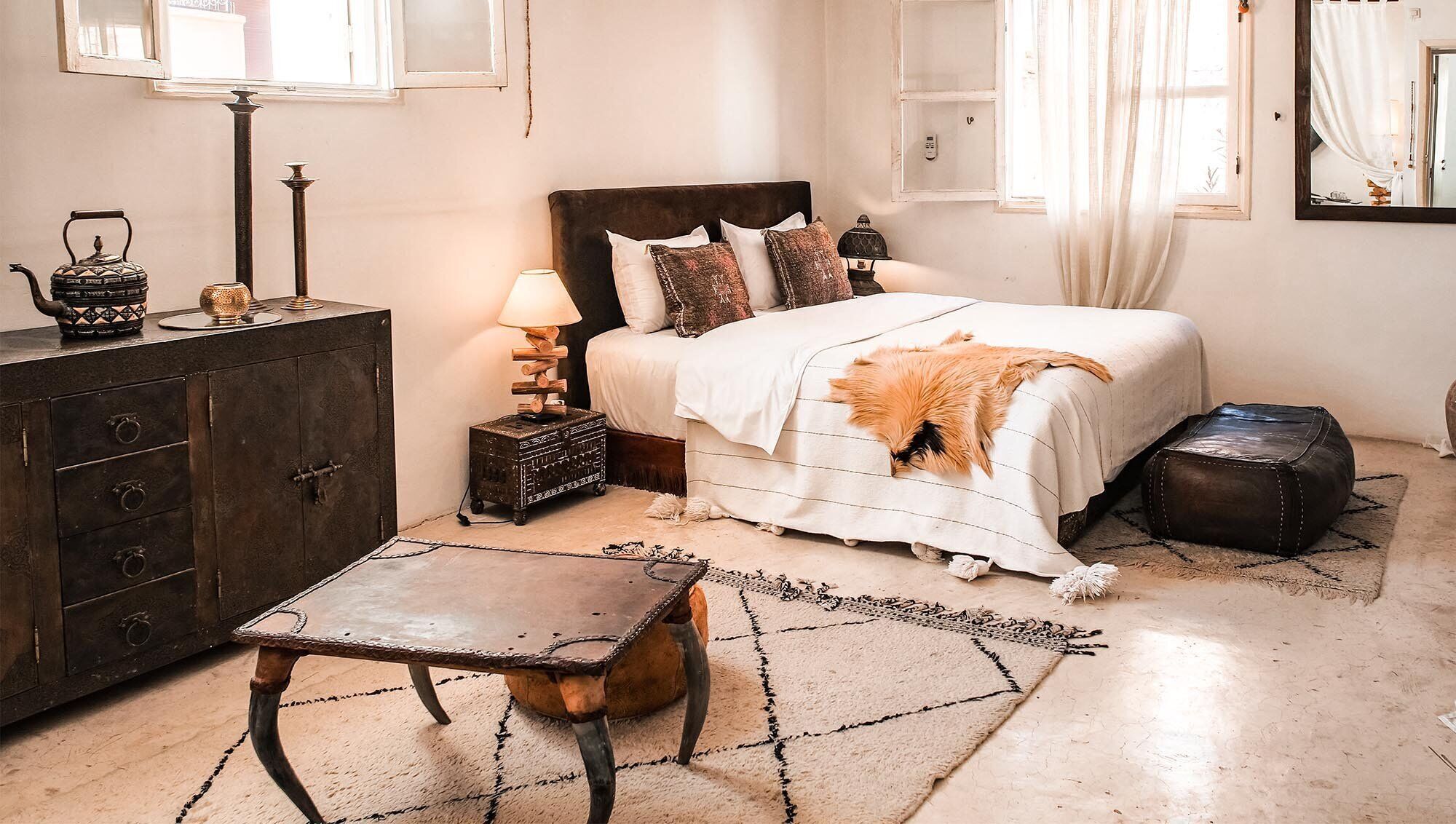 A bedroom with a bed, a dresser, a nightstand, a lamp, a rug, and a small table.