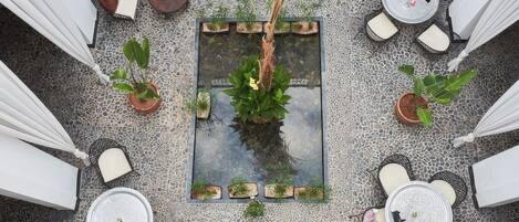 Vista cenital de un patio con varias zonas de estar, un elemento acuático central y plantas en macetas.