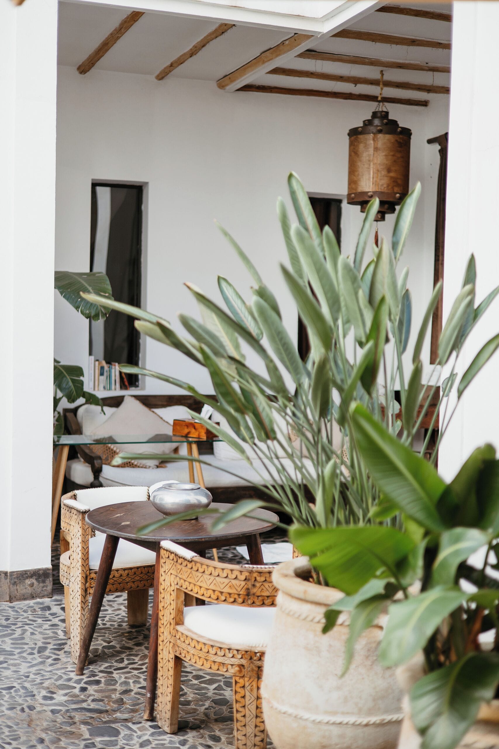 A cozy indoor seating area with wicker furniture, a hanging light fixture, and large potted plants.