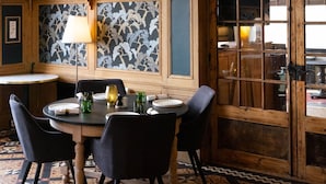 A dining area with a round table, black chairs, and patterned wall tiles. - Hôtel Restaurant Le Bellevue (La Bouille)