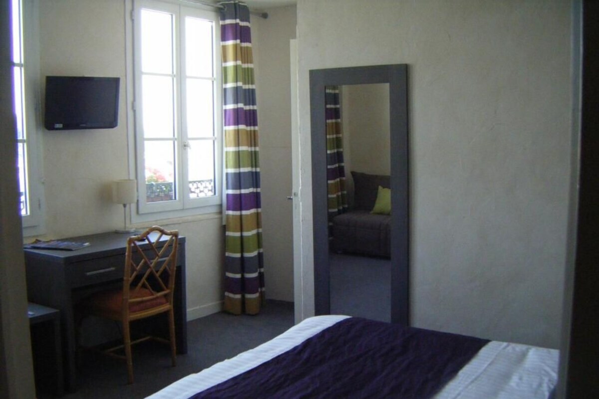 Un dormitorio con cama, escritorio, silla, televisor y ventana con cortinas.