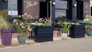An outdoor seating area with tables and chairs, potted plants, and a sign reading "LA TABLE J'Bector". - Hôtel Restaurant Le Bellevue (La Bouille)