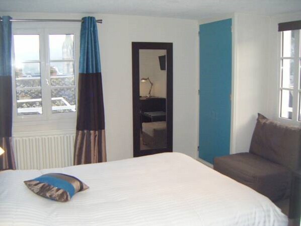 Una habitación de hotel con cama, una silla, un ventanal con cortinas y una puerta.
