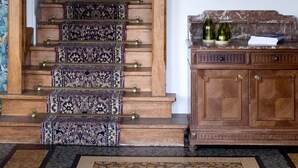 A staircase with patterned carpet and brass railings, leading to a room with a framed animal illustration wall and a wooden cabinet with bottles. - Hôtel Restaurant Le Bellevue (La Bouille)