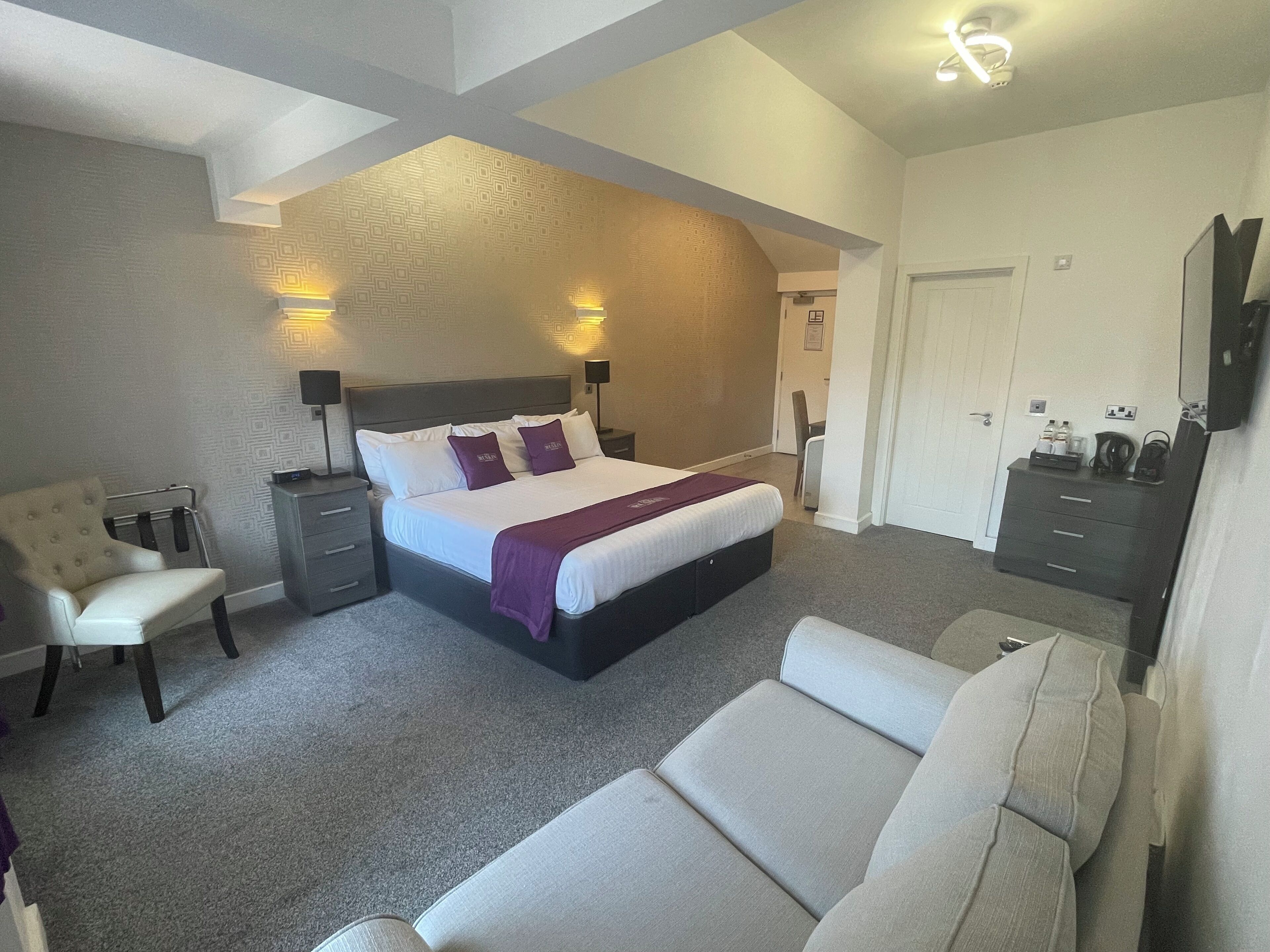 A modern hotel room with a large bed, a sofa, a desk, and a wardrobe.