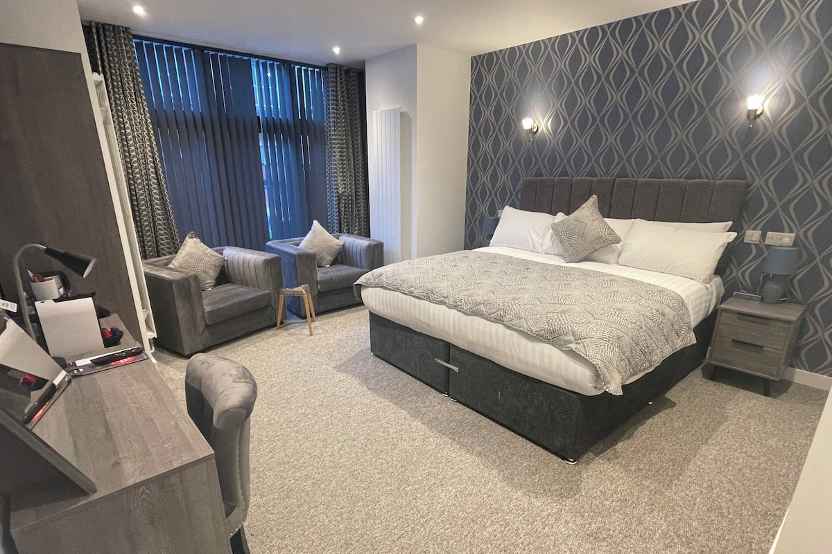 A modern bedroom with a large bed, a desk with a chair, a sofa, and a small table.