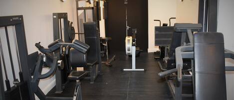 A gym with various exercise machines, a mirrored wall, and a door at the end.