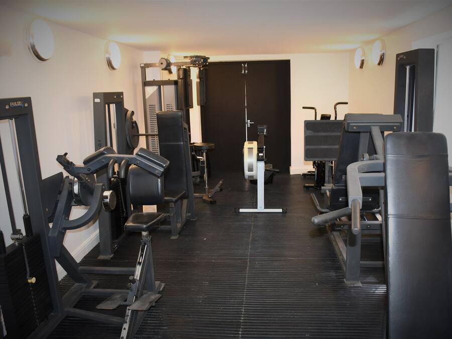 A gym with various exercise machines, a mirrored wall, and a door at the end.