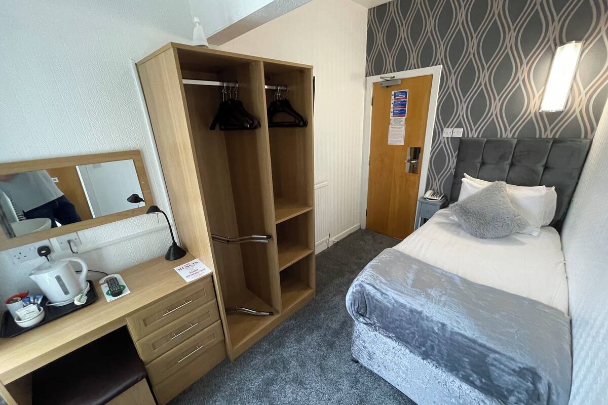 A hotel room with a bed, a desk with a computer, a wardrobe, and a bathroom door.