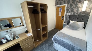 A hotel room with a bed, a desk with a computer, a wardrobe, and a bathroom door.