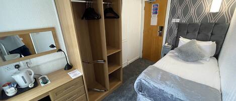 Una habitación de hotel con una cama, un escritorio con una computadora, un armario y la puerta del baño.