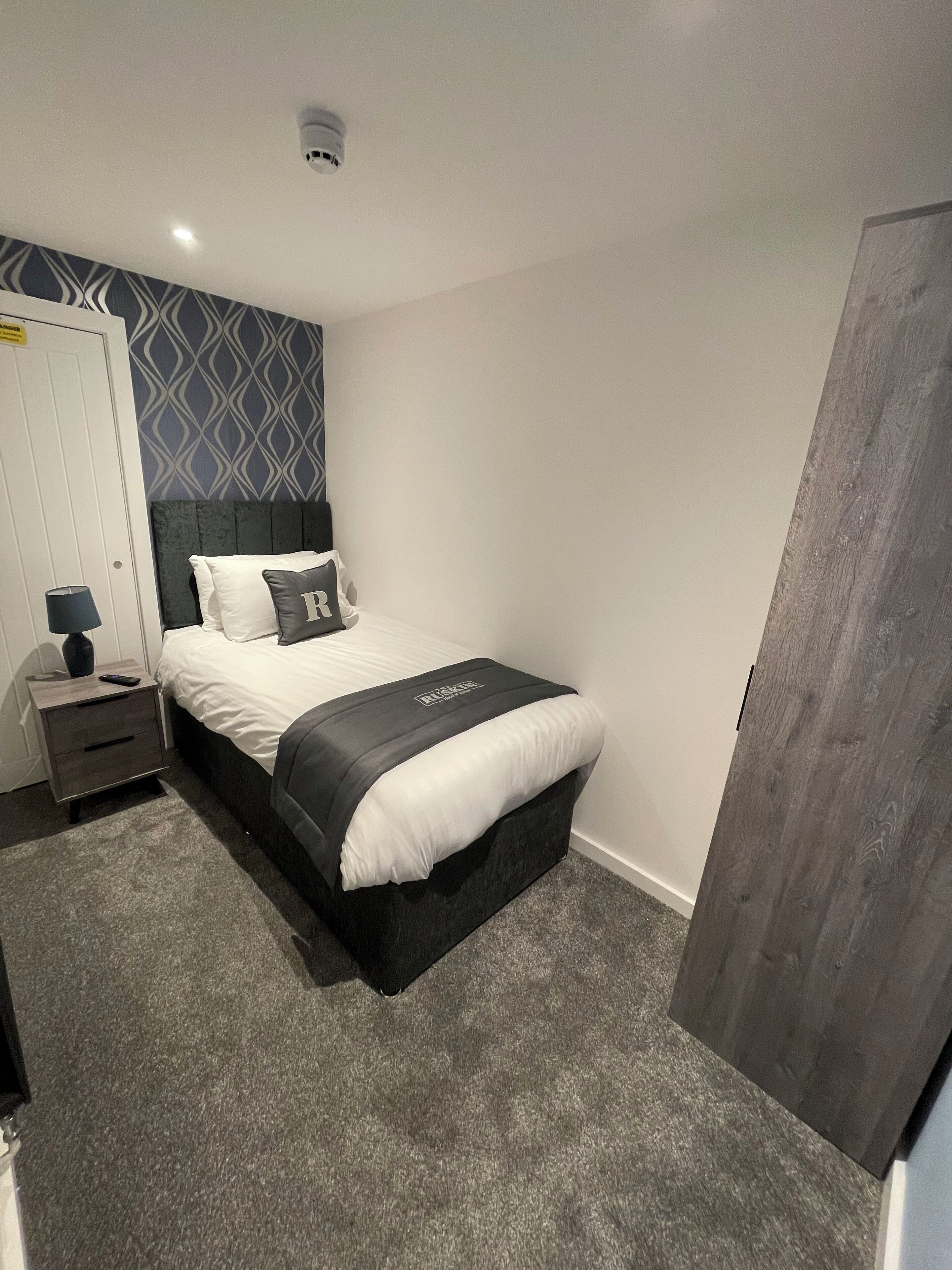 A neatly arranged bedroom with a bed, bedside table, and a wall-mounted light fixture.